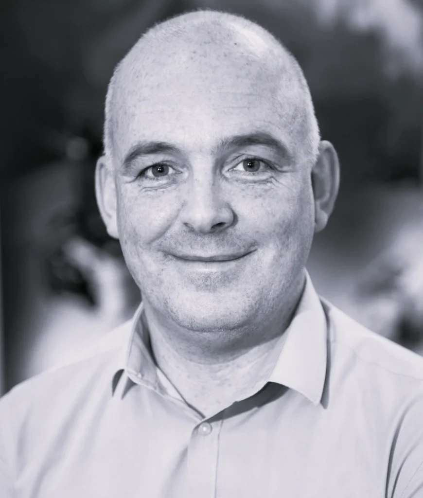 Photograph of a person with a blurred face, wearing a light-coloured collared shirt against a softly focused background. The image highlights the individual's upper body and head, with natural lighting and a neutral tone.